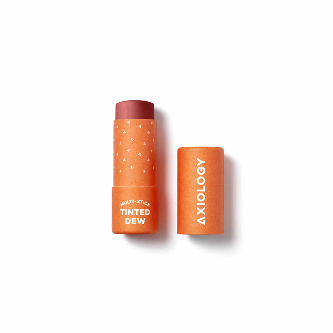 Axiologys Tinted Dew multi-stick, in a reddish-brown shade, is elegantly packaged in vibrant orange with white patterns. Its compostable packaging combines nourishing ingredients for a sustainable and versatile beauty experience.