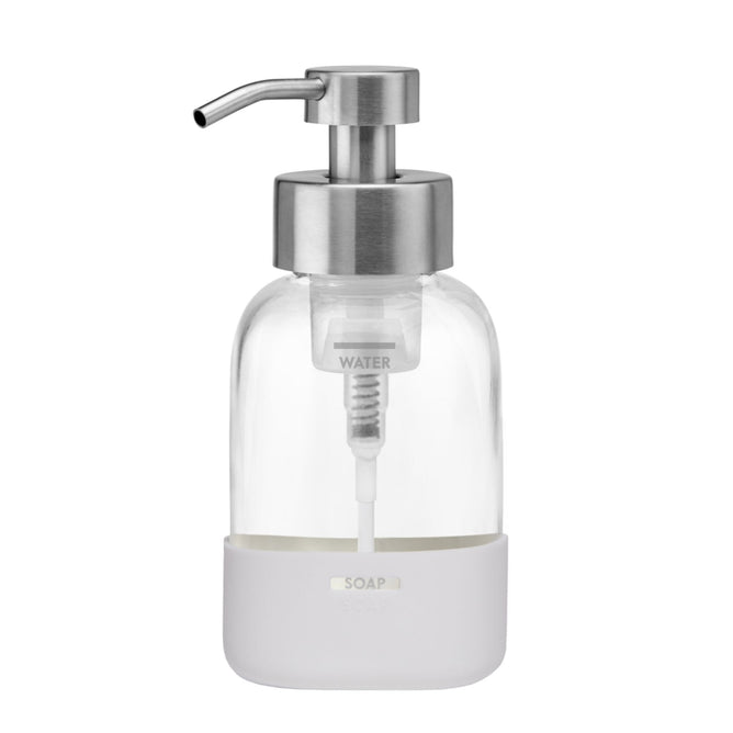 The Grove Co. Foaming Hand Soap Dispenser is a clear glass container with a silver pump and white base labeled SOAP, featuring a middle section marked WATER for content separation. Its designed for refilling, reducing plastic waste, and is perfect for your favorite Grove hand soap.