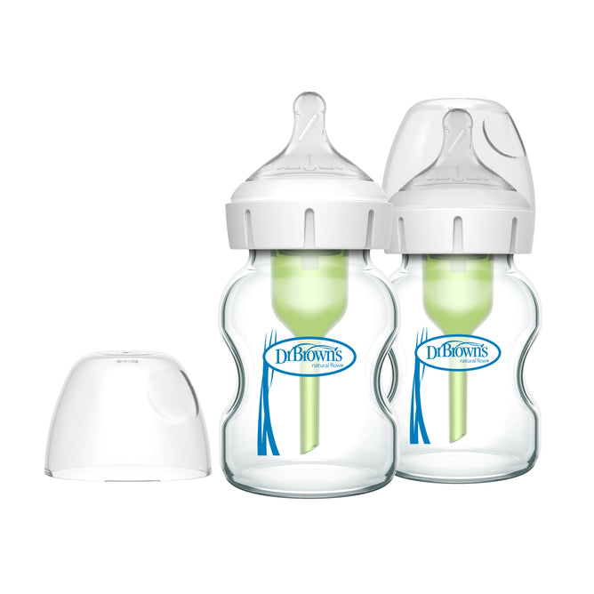 Two Dr. Browns Natural Flow Anti-Colic Options+ Wide-Neck Glass Baby Bottles include green internal vent systems, clear silicone Level 1 Slow Flow Nipples, and white caps with an extra cap shown separately. The bottles display a blue logo on the front.