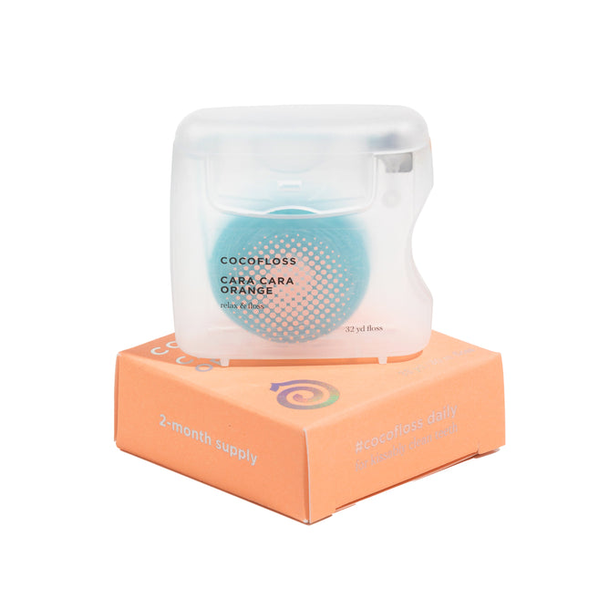 A clear container labeled Cocofloss Dental Floss rests on an orange box reading 2-month supply. The turquoise floss is recycled polyester and infused with coconut oil for soothing gums and effective plaque removal.