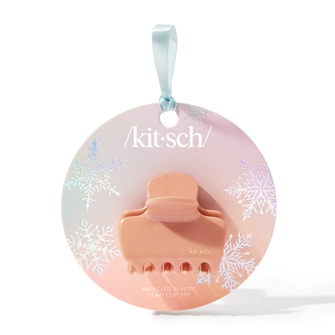 The Holiday Recycled Plastic Claw Clip by Kitsch is a peach medium-sized accessory packaged in a round pastel gradient box with snowflakes and a light blue ribbon, proudly displaying the brand name.
