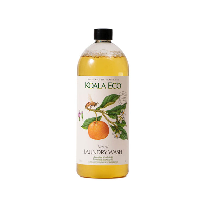 A bottle of Koala Eco Laundry Wash features orange and white blossoms, contains mandarin and peppermint, is biodegradable with plant-based ingredients and Australian essential oils, with an eco-friendly formula. It has a sleek black cap.