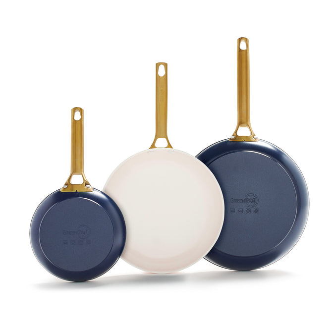 The GreenPan Reserve Ceramic Nonstick Fry Pans set includes three pans of varying sizes, each with gold handles. Two have navy-blue exteriors and one features a white interior. Each pan is marked with a circular logo and offers PFAS-free Thermolon ceramic nonstick surfaces for easy cooking.