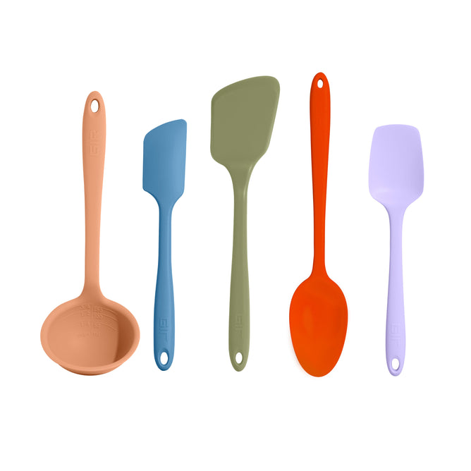 The 5-Piece Ultimate Tool Set from GIR includes a beige ladle, blue spatula, green slotted turner, orange spoon, and lavender scraper. Each heat-resistant silicone tool has a hanging hole at the handle end and is elegantly displayed in a row on a pristine white background.