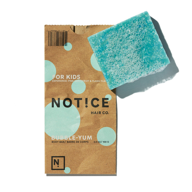 A vegan, cruelty-free Bubble-Yum Body Bar by NOT!CE Hair Co., scented with prickly pear and ylang-ylang, comes in a brown box with large light blue dots and sits beside a textured blue-green soap bar. Its kid-friendly and delightful.