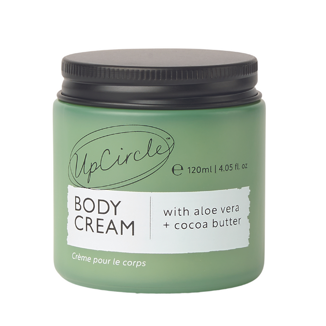 The green jar of UpCircle Body Cream with Aloe Vera + Cocoa Butter features 120 ml (4.05 fl. oz.) enriched with Date Seed, a black screw-on lid, and Crème pour le corps elegantly inscribed at the bottom for sophistication.