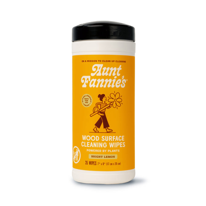 Aunt Fannies Wood Surface Wipes come in a cylindrical container with a bright orange label featuring a person sweeping flowers. These 35 lemon-scented wipes, infused with essential oils and a natural formula, rejuvenate surfaces effortlessly.