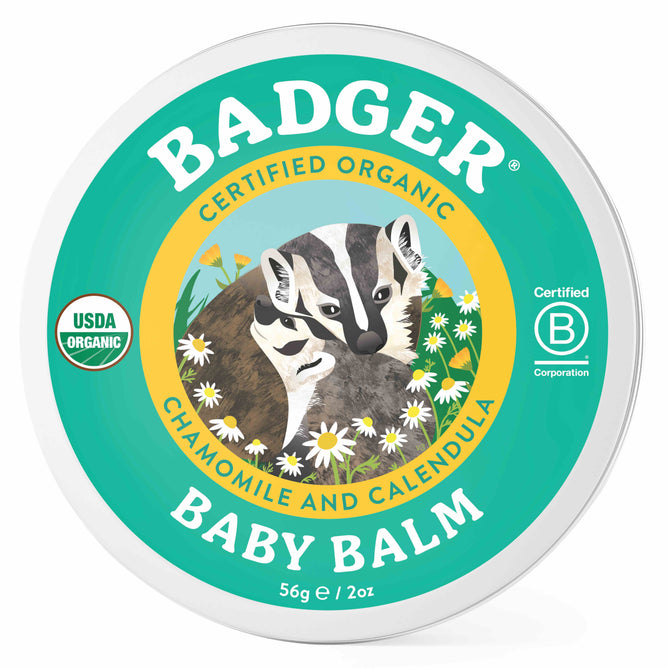 The image shows a round 56g/2oz tin of Badger Balm Baby Balm, ideal for babys sensitive skin. The lid has a green background with a badger illustration surrounded by daisies and is labeled Certified Organic with chamomile and calendula.