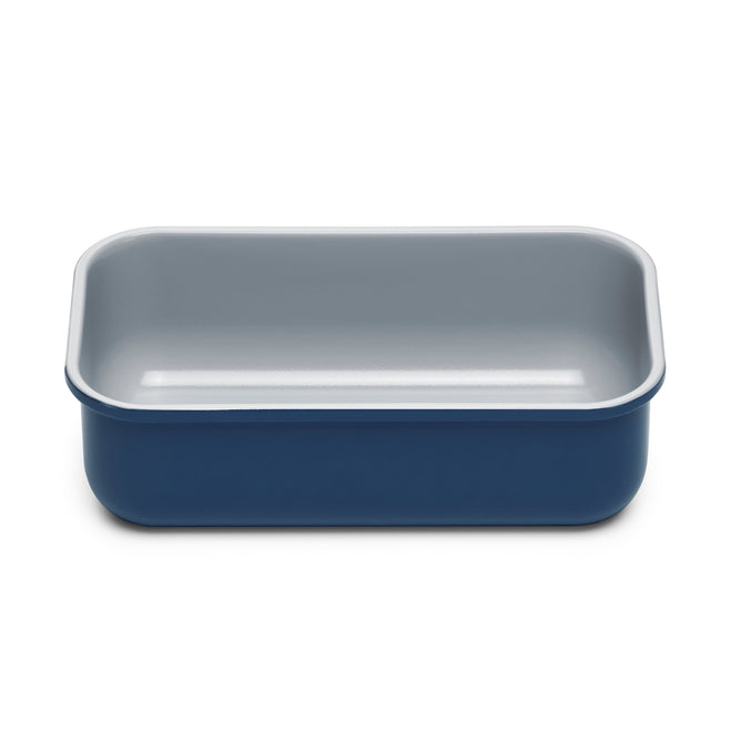 The Caraway Loaf Pan is a blue rectangular pan with rounded edges, featuring a light gray non-stick surface. Made of steel, it excels in baking and roasting. Set against a white background, this durable pan guarantees easy release and hassle-free cleanup each use.