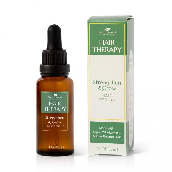 A 1 fl. oz (30 ml) amber dropper bottle of Hair Therapy Strengthen & Grow Hair Serum by Plant Therapy rests next to its green and white box, highlighting botanical ingredients like Argan Oil and Vitamin E, designed to naturally strengthen and grow hair.