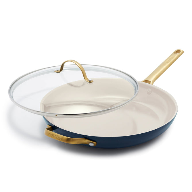 The GreenPan Reserve Ceramic Nonstick Fry Pan with Lid, 12, features a dark exterior and light interior, accented by gold-colored handles. The glass lid includes a gold handle, and the skillet sits elegantly on a pristine white surface.