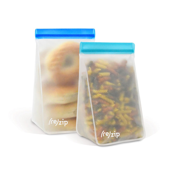 The Stand-Up Tall - 6 & 8 Cup Pantry Bag Kit by (re)zip features two translucent, reusable bags with blue zips. The left bag holds bagels, the right has colorful pasta. Made from food-safe PEVA, these bags stand upright, display the (re)zip logo, and help reduce plastic waste.