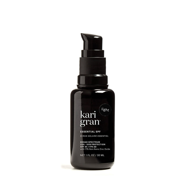 A black pump bottle labeled Kari Gran Essential Tinted SPF 30 contains a mineral sunscreen offering broad-spectrum UVA/UVB protection and 15% non-nano zinc oxide, infused with red raspberry seed oil. It provides light coverage in a NET 1 FL OZ / 30 ML size.