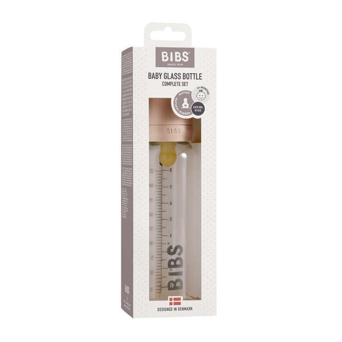 The BIBS Glass Baby Bottle Complete Set features charming beige packaging with a dotted pattern. A clear window reveals the durable borosilicate glass bottle with measurement markings. The top panel showcases the logo, product details, an anti-colic function, and has a convenient carrying handle.