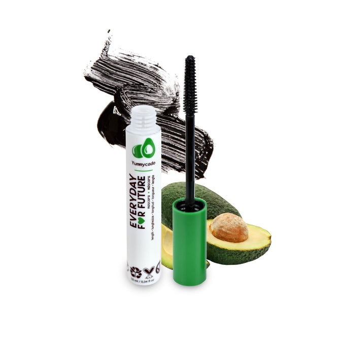 A tube of Lengthening Avocado Mascara, with an open applicator brush stands upright, showcasing green branding and Everyday For Future. Behind it, mascara strokes and half an avocado emphasize its natural theme, infused with Organic Avocado Oil to support lash growth.