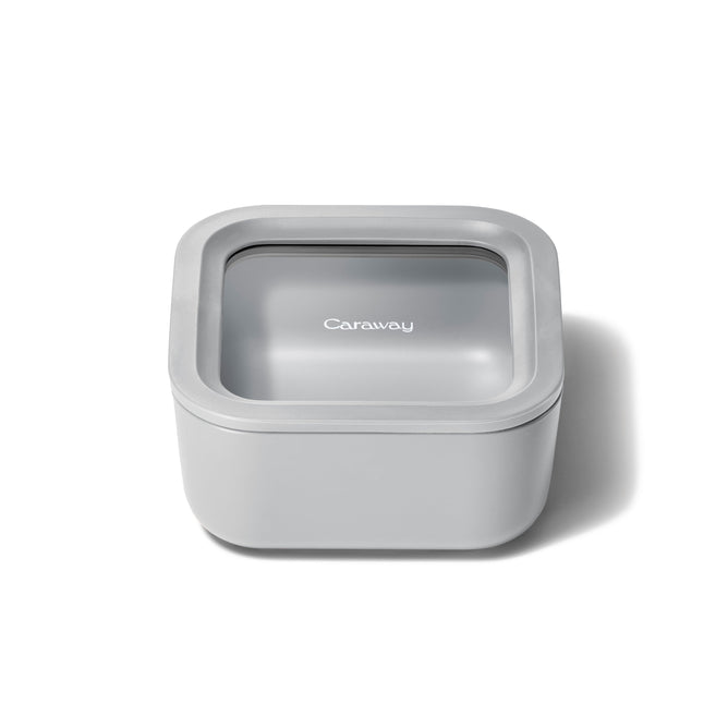 A small, square, light gray food container by Caraway features a snug-fitting ceramic-coated glass lid with Air Release technology, combining a sleek modern design for optimal freshness.