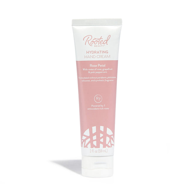 Rooted Beauty Hydrating Hand Cream in Rose Petal scent, packed with plant-based moisturizers and shea butter, comes in white and pink packaging highlighting pink grapefruit and pink peppercorn. Perfect for dry skin, this 2 fl oz (59 mL) cream offers lush hydration.