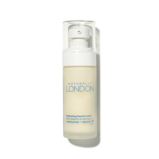 A clear bottle of Naturally Londons Hydrating Hand Cream, enriched with Red Raspberry Seed Oil, wakame, and quinoa protein. The white pump and cap accompany vibrant blue brand details on the packaging.