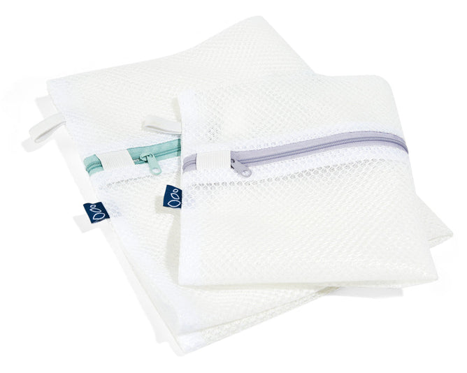 Two overlapping Grove Co. Laundry Delicates Bags, ideal for delicates, rest on a white surface; the larger bag has a green zipper, and the smaller one has a gray zipper. Both reusable bags feature small black tags.
