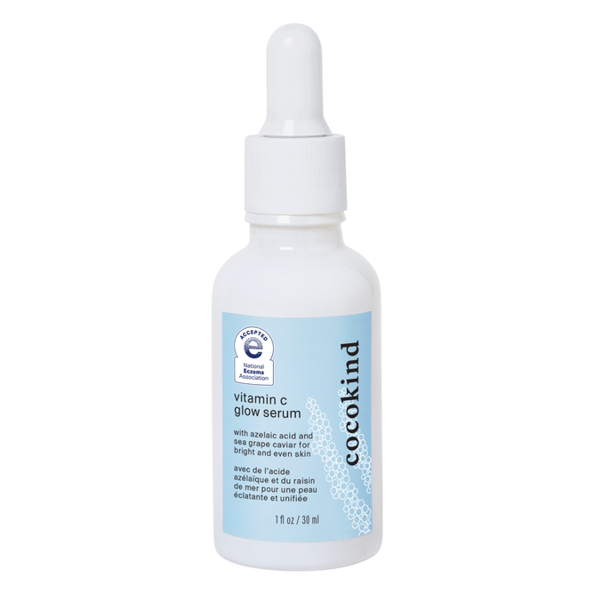 A white dropper bottle of Cocokinds Vitamin C Glow Serum features a light blue label displaying the product name, a small illustration, and details highlighting its benefits for brightening and evening skin tone, with azelaic acid for clarity and smoothness.