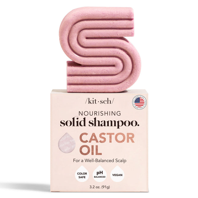 A pink S-shaped shampoo bar sits on a box marked Kitsch Castor Oil Nourishing Shampoo Bar. Ideal for color-treated hair, the box highlights icons for Color Safe, pH Balanced, and Vegan. The product weighs 3.2 oz (91g).