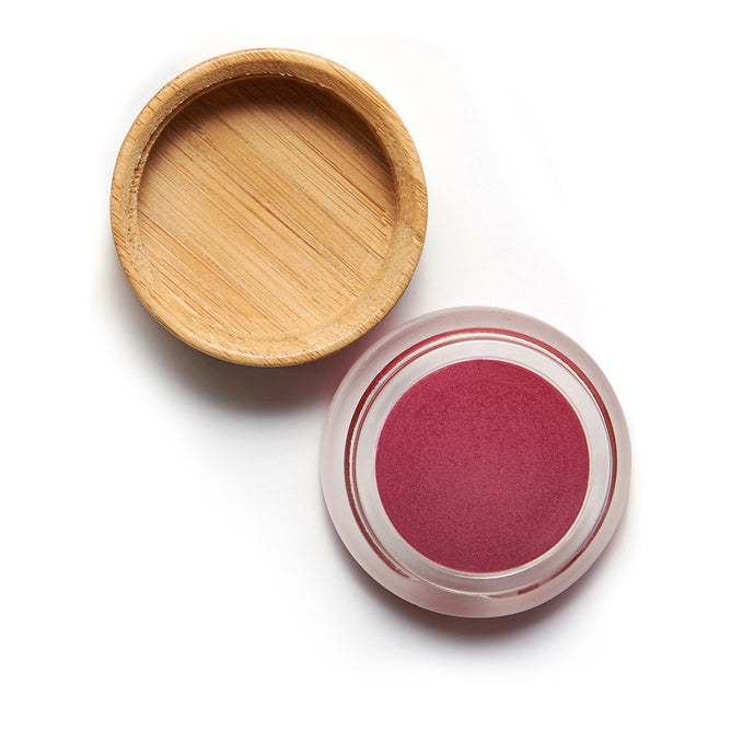 A small round clear container with an open wooden lid beautifully showcases the rich pink hue of Mad Hippies mineral-tinted Cheek & Lip Tint against a light background.