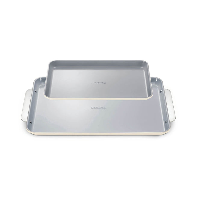 The Caraway Ceramic Baking Sheet Duo features two overlapping sheets with white edges and light gray, naturally non-stick surfaces, complete with extended side handles for easy grip. They boast a non-toxic design perfect for healthy baking and are set against a white background.