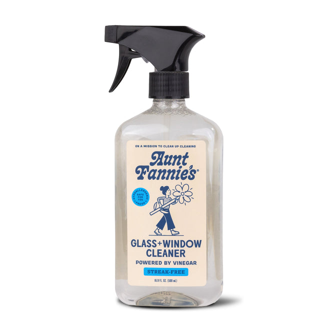 Aunt Fannies Glass & Window Cleaner comes in a clear spray bottle with a black nozzle, featuring blue text and a graphic of a person holding a flower. This plant-based cleaner, powered by vinegar, provides a streak-free shine.