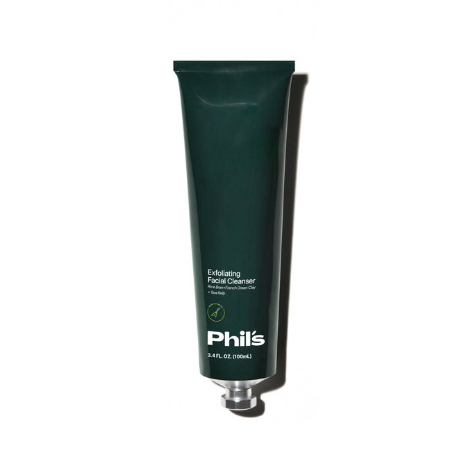A dark green tube labeled Exfoliating Facial Cleanser by Phils, enriched with French green clay and adorned with leaf illustrations, stands upright against a plain white background.