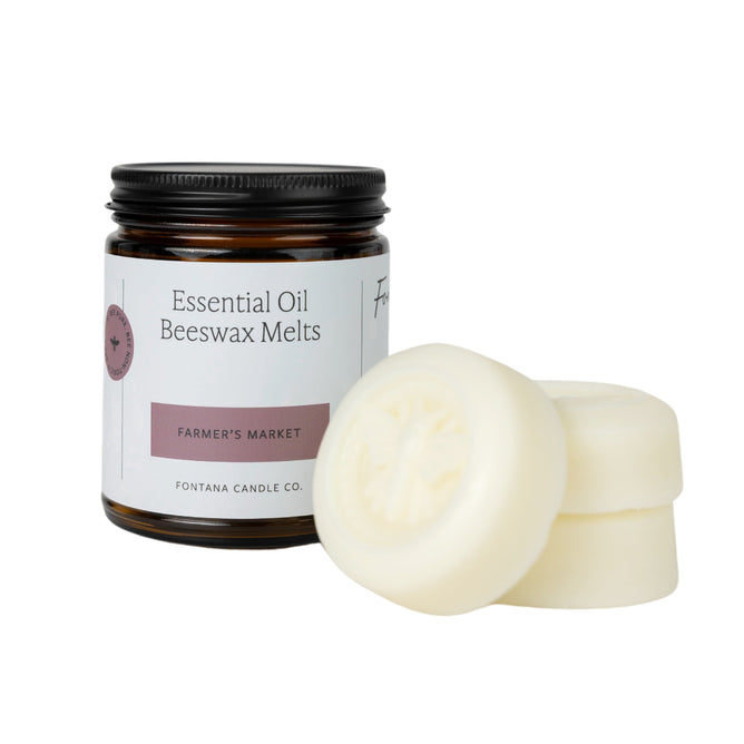 A dark glass jar labeled Essential Oil Beeswax Melts - Farmers Market by Fontana Candle Co. sits next to three off-white wax melts, each with a subtle floral imprint on top.