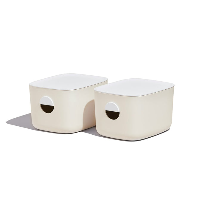 Two Medium Storage Bins from Open Spaces, featuring beige rectangular design and circular handles, elegantly sit on a pantry shelf. With their soft shadows, these bins are perfect for multi-purpose storage.