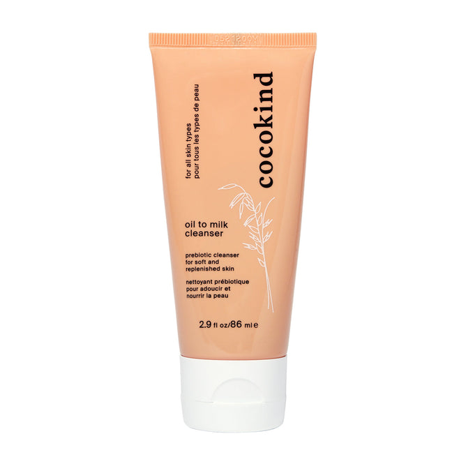 Image of a peach-colored Cocokind Oil to Milk Cleanser tube with black text detailing branding and product information, including probiotic cleanser and for soft and replenished skin. The organic formula features fermented oat oil blend. Tube size: 2.9 fl oz/86 ml.