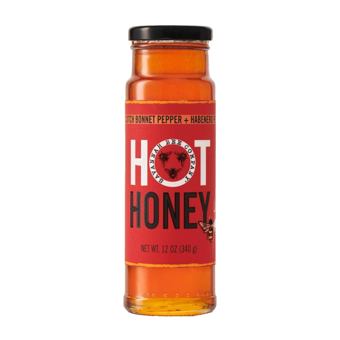 Savannah Bee Companys Hot Honey is a 12 oz (340 g) glass bottle of amber-colored acacia honey infused with scotch bonnet and habanero peppers. The red label features illustrations of bees, peppers, and the words Hot Honey.