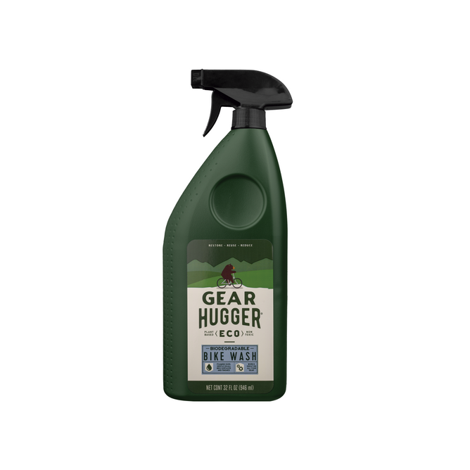 A dark green 32 fl oz (946 ml) spray bottle from Gear Hugger, labeled Eco Bike Wash, features a mountain biking scene. It includes a black spray nozzle and emphasizes a non-toxic formula that cleans your bike while reducing environmental impact.