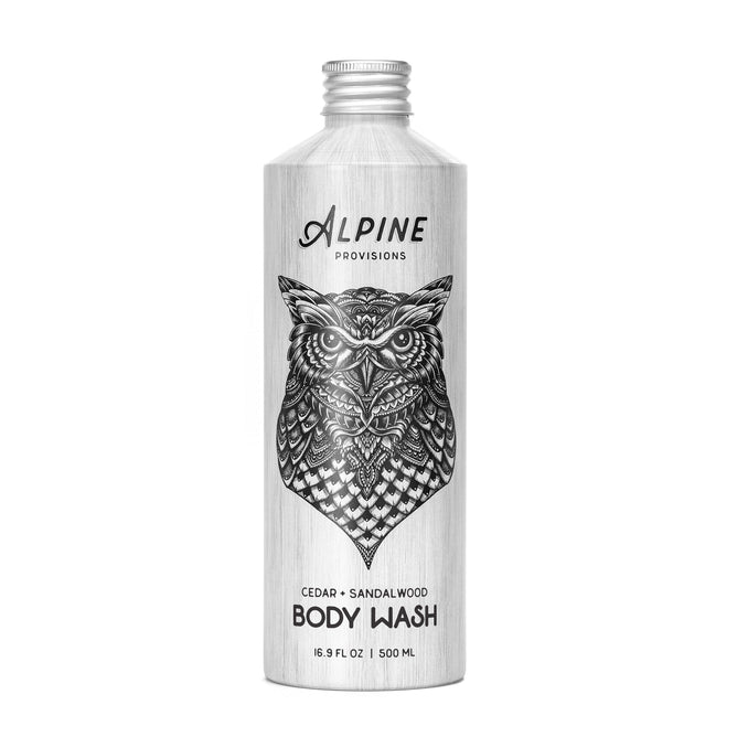 A silver bottle of Alpine Provisions Body Wash features a detailed black owl design, labeled Cedar & Sandalwood Body Wash, 16.9 fl oz / 500 ml, crafted with sustainably-sourced essential oils evoking an alpine forest.