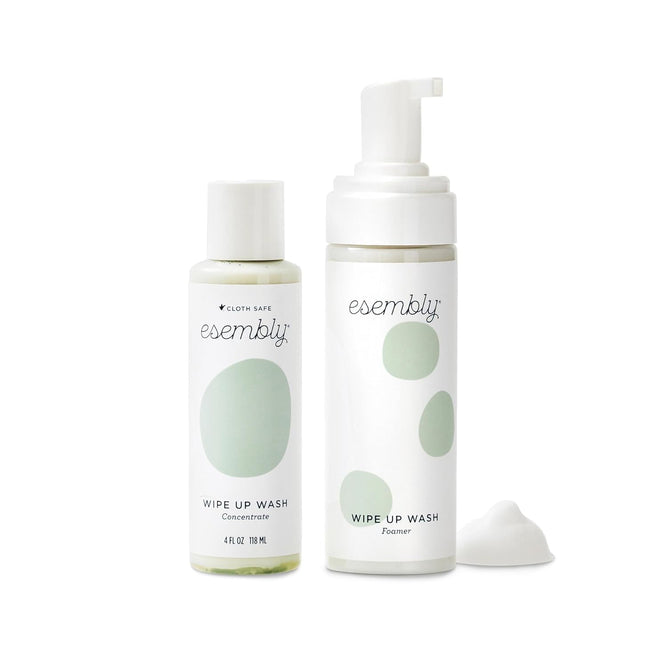 The Wipe-Up Wash Kit by Esembly Baby includes two bottles with white labels and green dot designs: one features Wipe Up Wash Concentrate with a screw cap, and the other is a Wipe Up Wash Foamer with a pump dispenser, perfect for organic foaming cleanser use with cloth wipes.