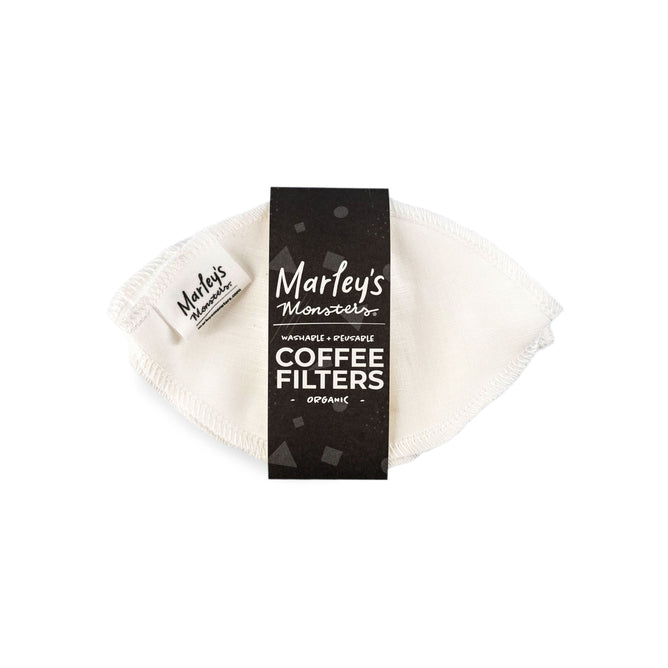A white, reusable coffee filter made from organic unbleached linen with visible stitching is partially wrapped in black packaging, labeled Marleys Monsters, Reusable Coffee Filters: Basket, promoting a plastic-free coffee experience.