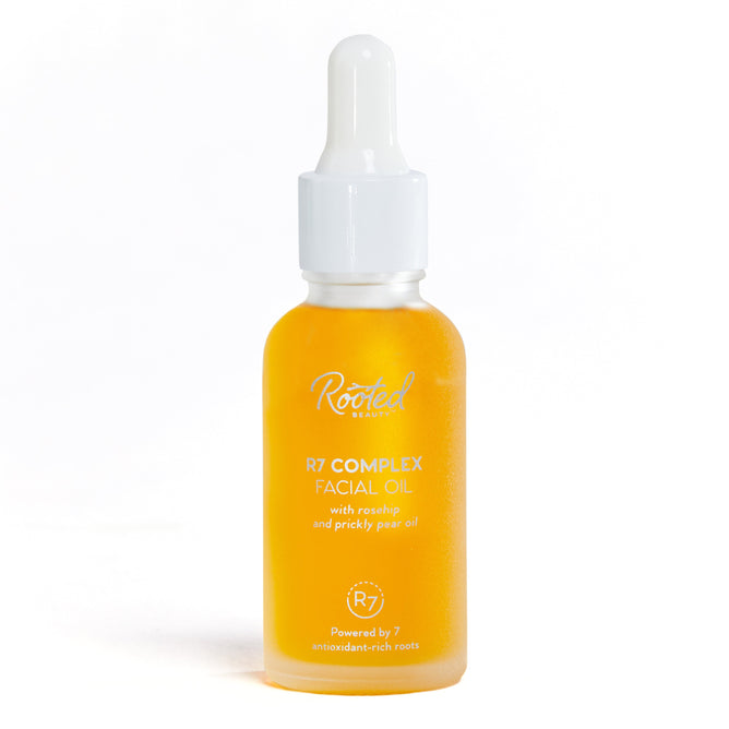 The R7 Complex Facial Oil by Rooted Beauty features a glass dropper bottle with antioxidant-rich yellow liquid, boasting deep hydration from rosehip and prickly pear oils. The simple design sits elegantly against a plain white background.