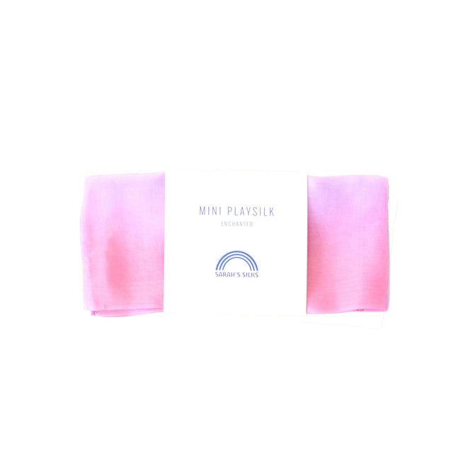 The Mini Playsilk by Sarahs Silks features a pink and lavender gradient perfect for imaginative play. It comes folded with a rainbow logo and is crafted from 100% pure silk, labeled as MINI PLAYSILK, ENCHANTED.