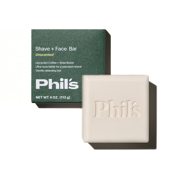 A square bar of Phils soap, featuring Phils embossing, rests under green packaging labeled: Shave + Face Bar, Unscented, Upcycled Coffee Oil + Shea Butter. Ultra-luxe lather for a precision shave. Gentle cleansing bar. NET WT 4 OZ. (113 g).