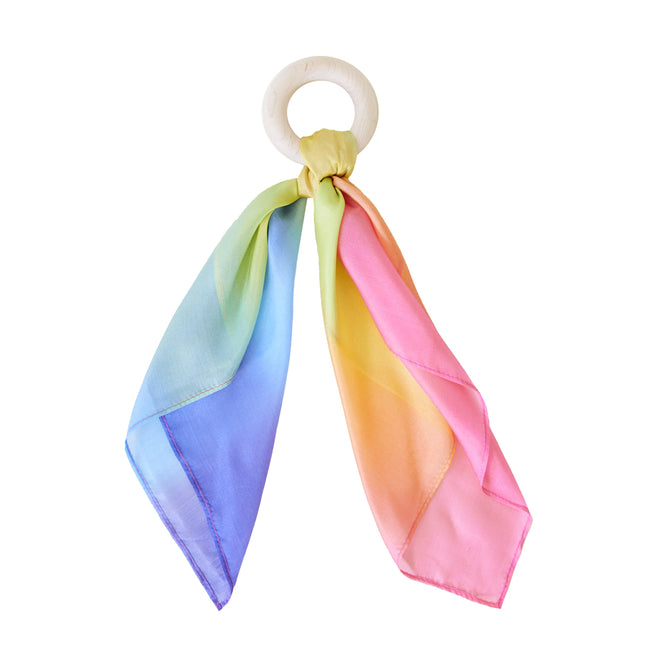 Sarahs Silks offers a Silk and FSC-Certified Wood Baby Teether featuring a multicolored silk scarf in blue, green, yellow, and pink tied to a solid wood ring with eco-friendly dyes, combining elegance with sustainability.
