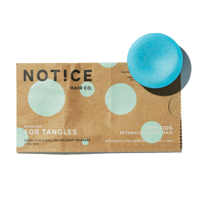 A brown package labeled NOT!CE Hair Co For Tangles Conditioner Bar rests under a round, blue bar. Designed for kids hair, it detangles fine hair with a refreshing pink grapefruit and ylang ylang scent.