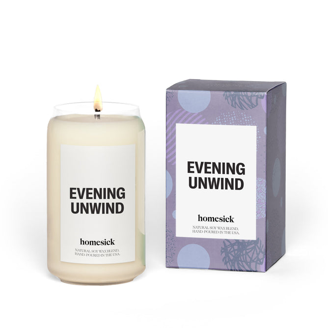 A lit Evening Unwind candle from Homesick, crafted from natural soy wax with calming lavender scents, sits beside a matching box with purple and white design, providing a soothing escape.