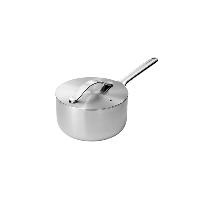 The Caraway Stainless Steel Sauce Pan, 3 qt, features a minimalist design with a long handle and fitted lid. Made from non-toxic stainless steel, its sleek silver finish is complemented by a small hanging hole and durable 5-ply construction, emphasized against its light background.