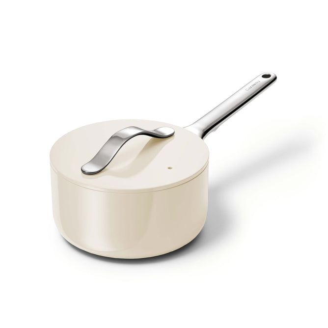 The Caraway Ceramic Sauce Pan, 1.75 qt in cream, features a non-stick surface and a shiny stainless steel handle. Its lids smooth, modern design ensures style meets functionality, making it ideal for healthy cooking against a white backdrop.