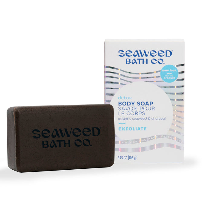 A 3.75 oz/106g bar of Detox Exfoliating Body Soap from The Seaweed Bath Co features a wavy, iridescent design and rests in front of packaging labeled Detox Body Soap, Atlantic Seaweed & Charcoal, infused with bladderwrack seaweed extract for exfoliation.