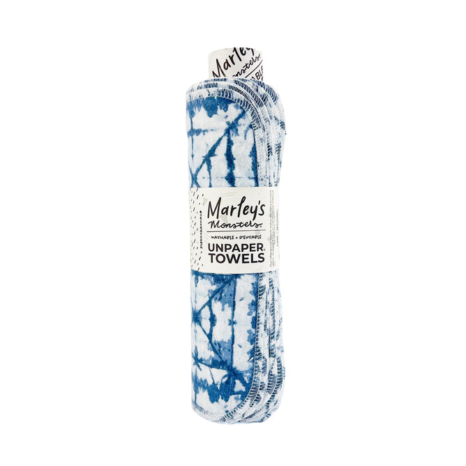 The Rolled Unpaper® Towels by Marleys Monsters feature a blue and white tie-dye pattern. These eco-friendly, reusable cloths are rolled up and secured with a label displaying the brands logo.