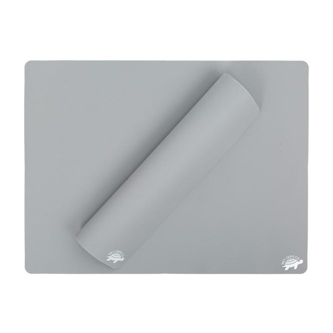 A gray, food-grade silicone baking mat from Net Zero Co.s Reusable Baking Un-Paper collection is laid flat with a corner rolled over. The surface features a small hedgehog logo in the bottom-right corner, providing an eco-friendly alternative to parchment paper.