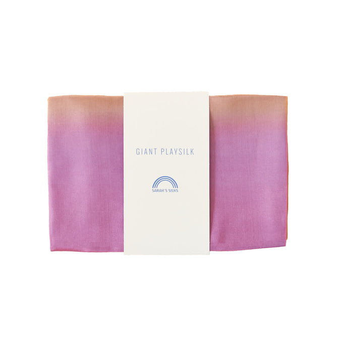 A folded silk fabric transitioning from orange to pink is wrapped with a white label reading Sarahs Silks Giant Playsilk for Open-Ended, Imaginative Play, featuring a small rainbow logo, ideal for Montessori & Waldorf-inspired play.