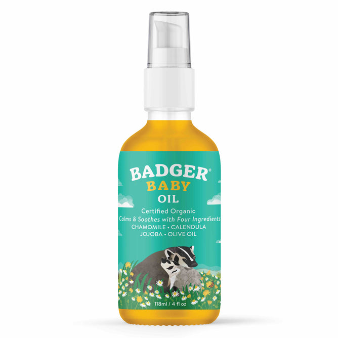 A 118 ml bottle of Badger Balm Baby Oil with a pump dispenser has a forest and sky design, featuring a badger, flowers, and text stating Certified Organic, Chamomile, Calendula, Jojoba, Olive Oil. This gentle moisturizer is made with organic ingredients.
